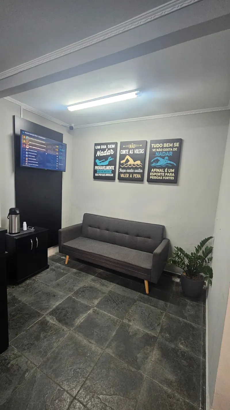Sala de espera com sofá, TV e quadros motivacionais de natação